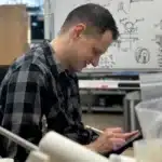 A happy in2being employee drawing on an iPad with product sketches on a whiteboard in the background