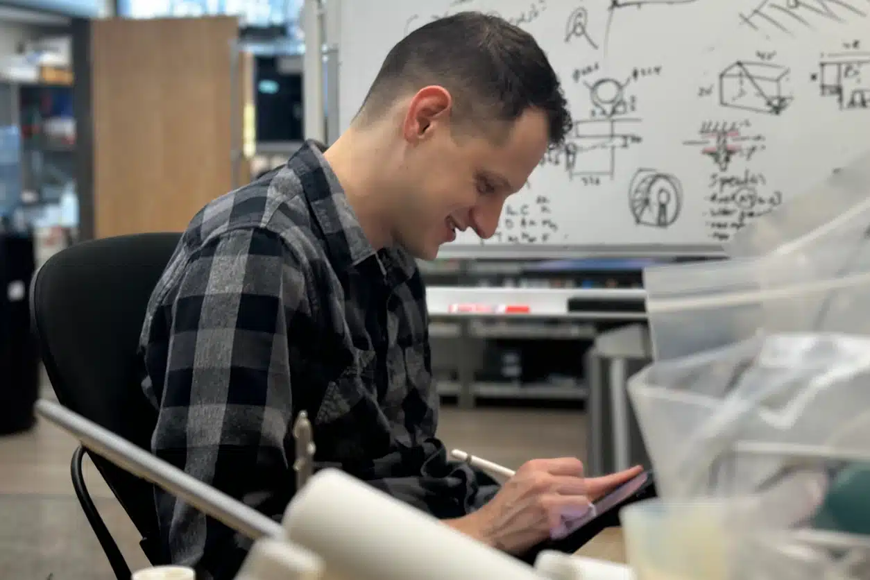 A happy in2being employee drawing on an iPad with product sketches on a whiteboard in the background